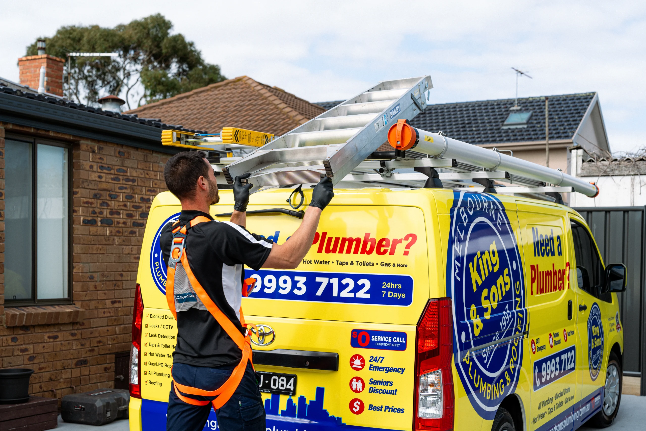 Plumber loading a ladder onto a King and Sons Plumbing service van, stormwater and roof access equipment